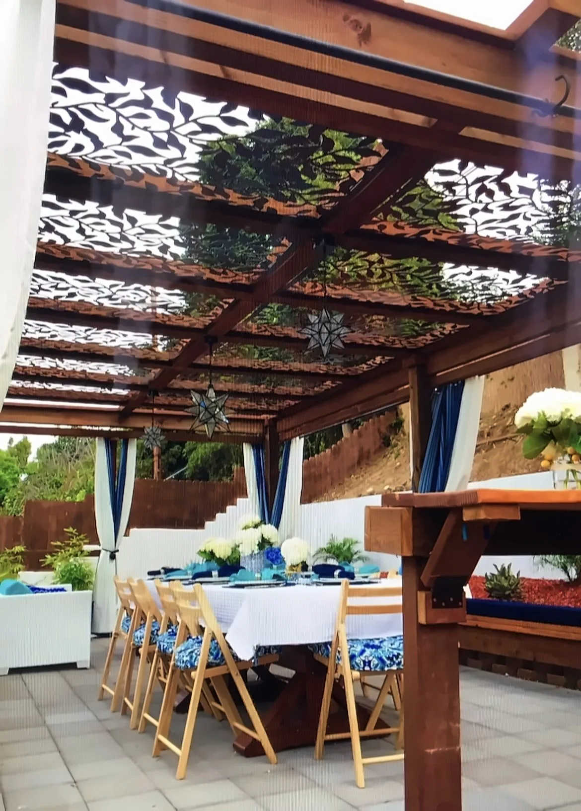 Timber pergola with laser-cut leaf canopy panels over an outdoor dining table